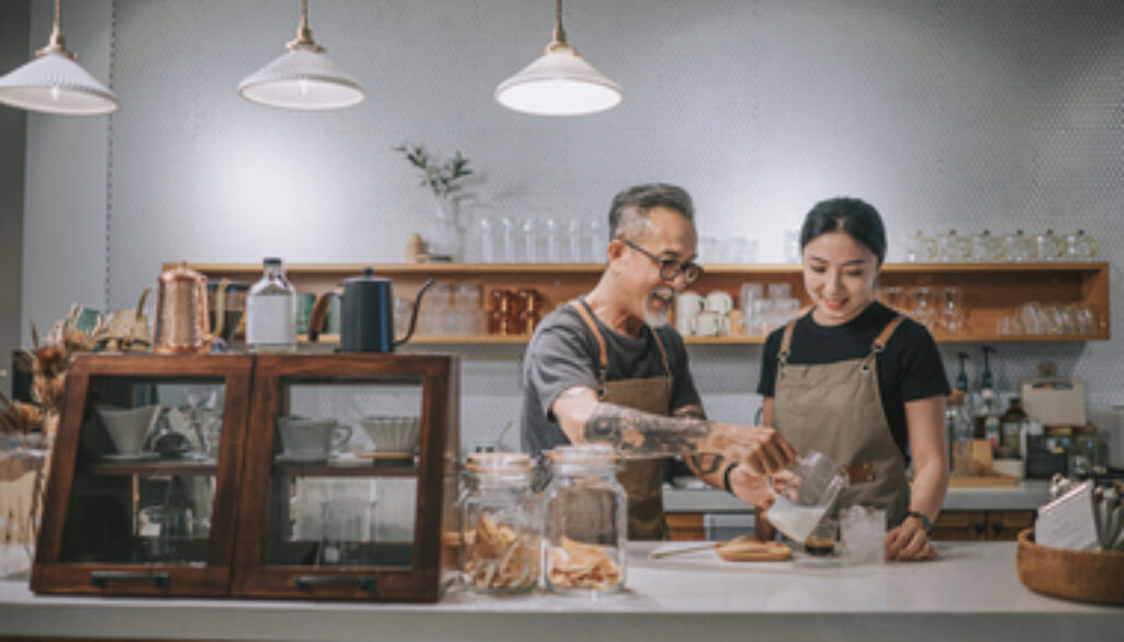 asian chinese senior male barista teaching his daughter making coffee at cafe bar counter