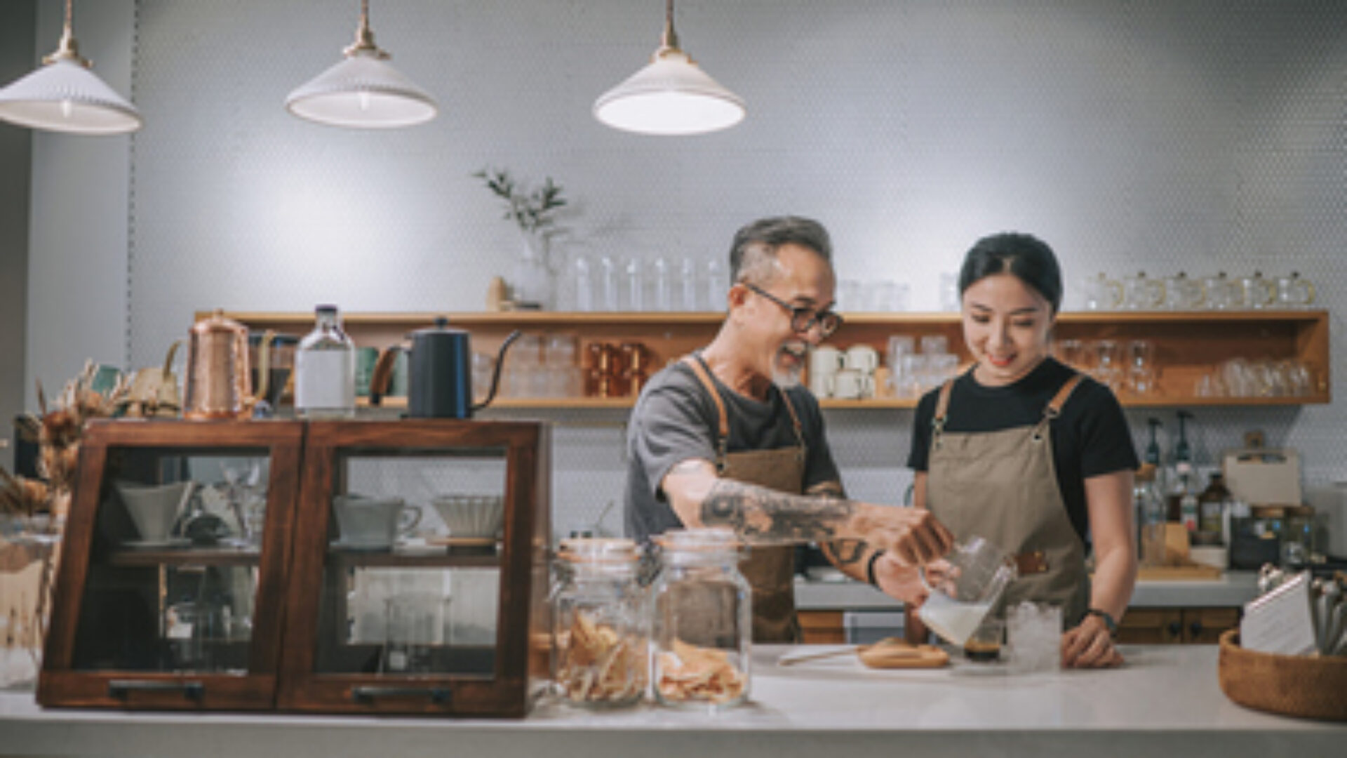 asian chinese senior male barista teaching his daughter making coffee at cafe bar counter