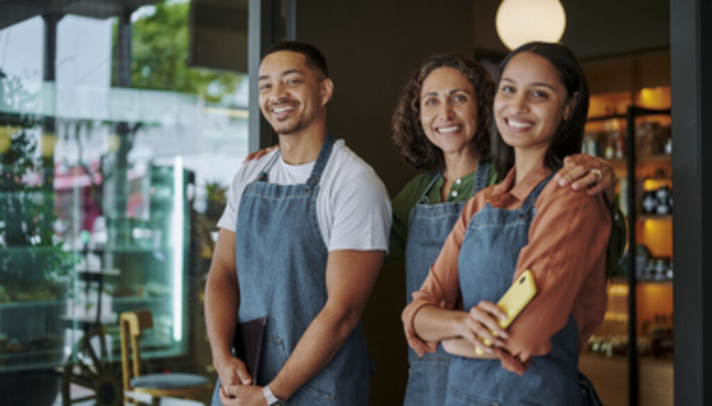 Deli owner and two employees smiling at the door to her shop