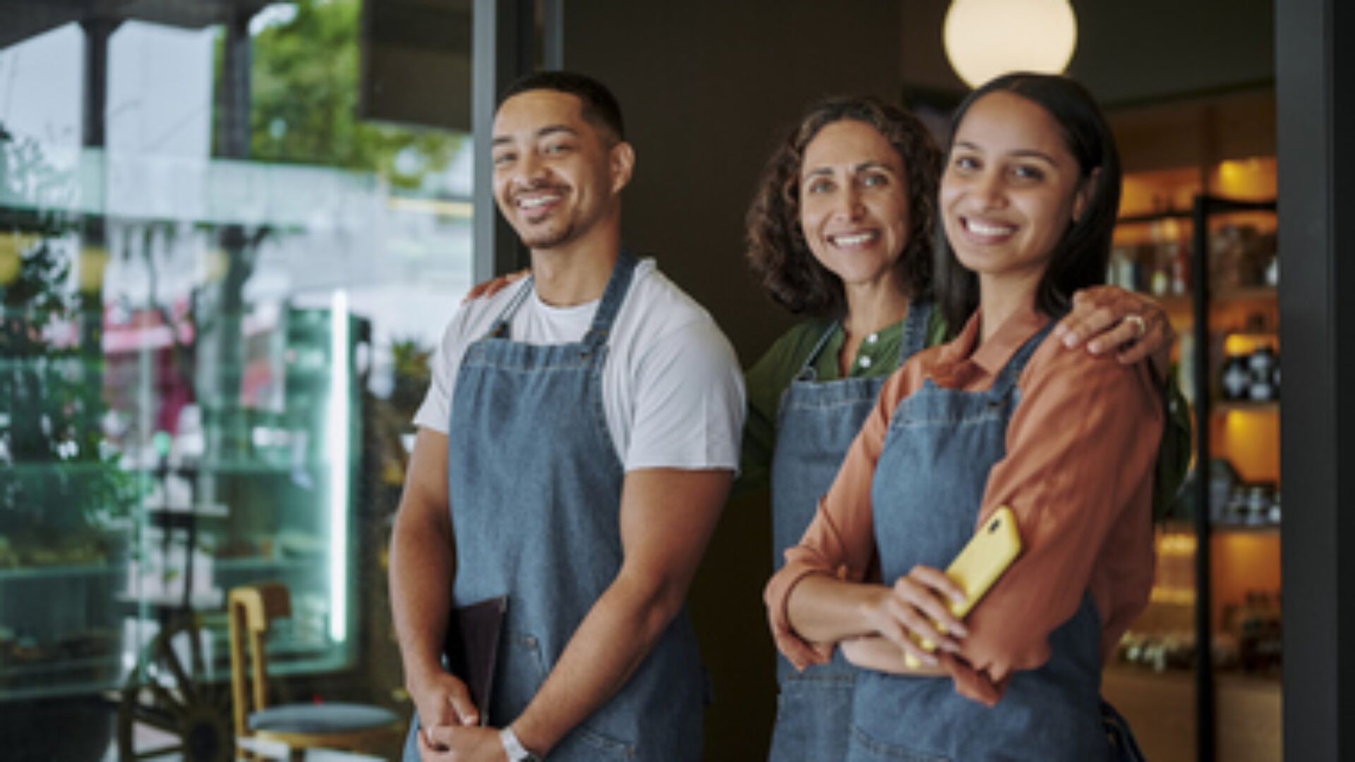 Deli owner and two employees smiling at the door to her shop