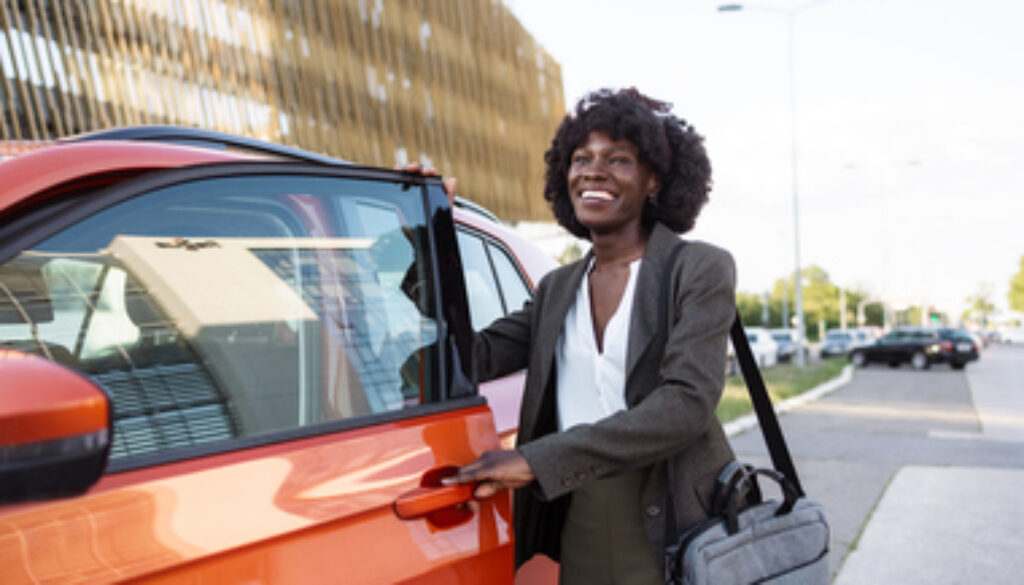 Cheerful businesswoman opening car door in urban area