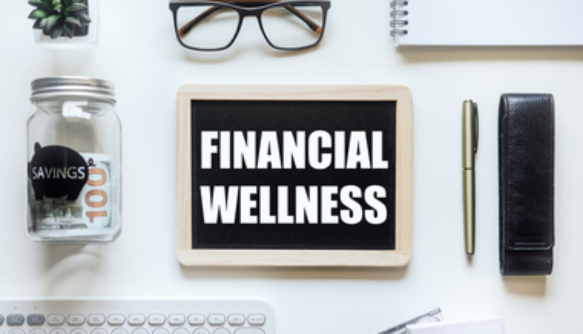 Financial Wellness. Black frame with word Financial Wellness on table with mason jar saving bank, stationery and glasses. Investment in life insurance and healthcare concept