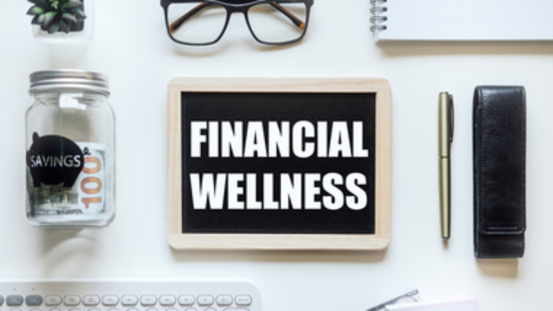 Financial Wellness. Black frame with word Financial Wellness on table with mason jar saving bank, stationery and glasses. Investment in life insurance and healthcare concept