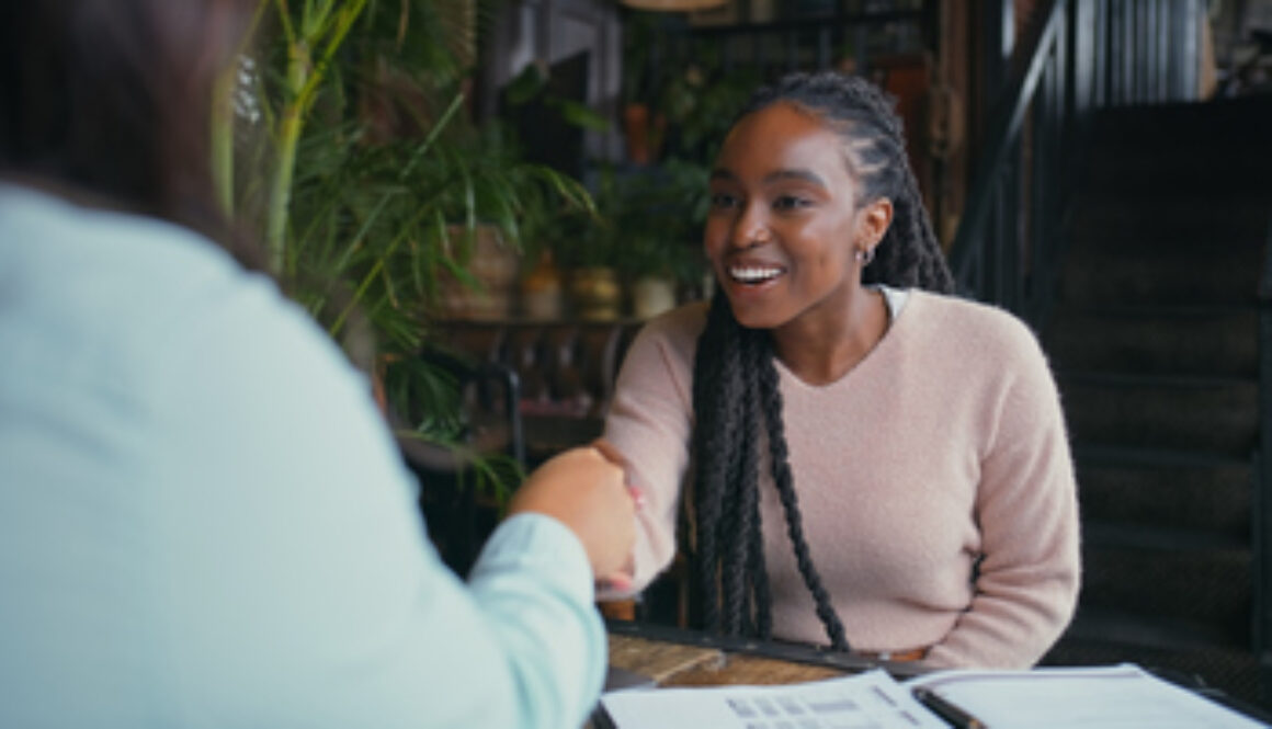 Happy woman, handshake and interview with intern at cafe for meeting, hiring or recruiting opportunity. Female person, employer and candidate shaking hands with smile for career or job at coffee shop