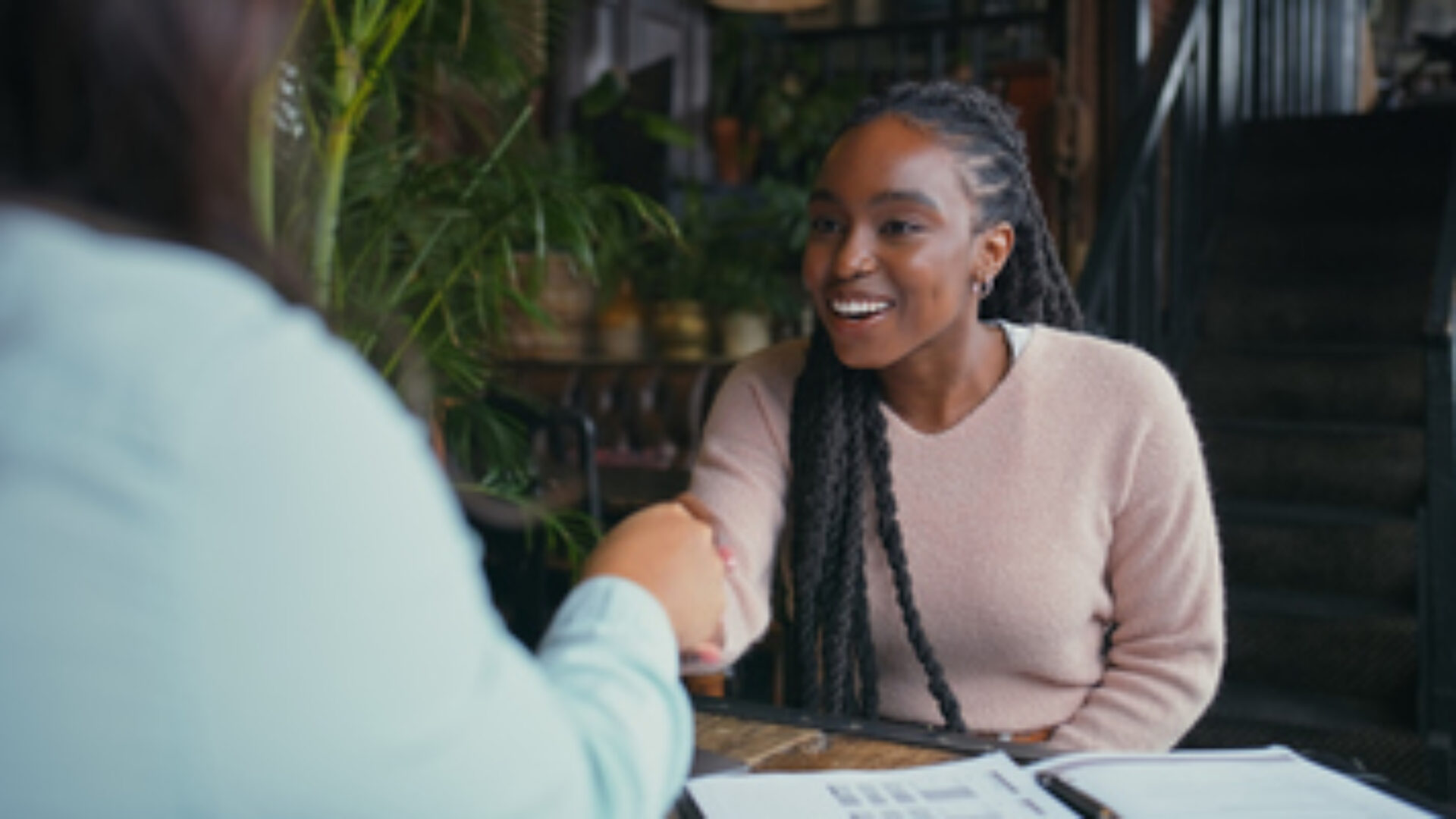 Happy woman, handshake and interview with intern at cafe for meeting, hiring or recruiting opportunity. Female person, employer and candidate shaking hands with smile for career or job at coffee shop