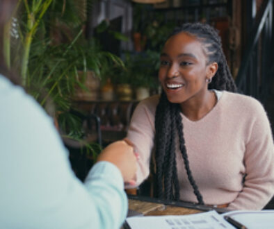 Happy woman, handshake and interview with intern at cafe for meeting, hiring or recruiting opportunity. Female person, employer and candidate shaking hands with smile for career or job at coffee shop