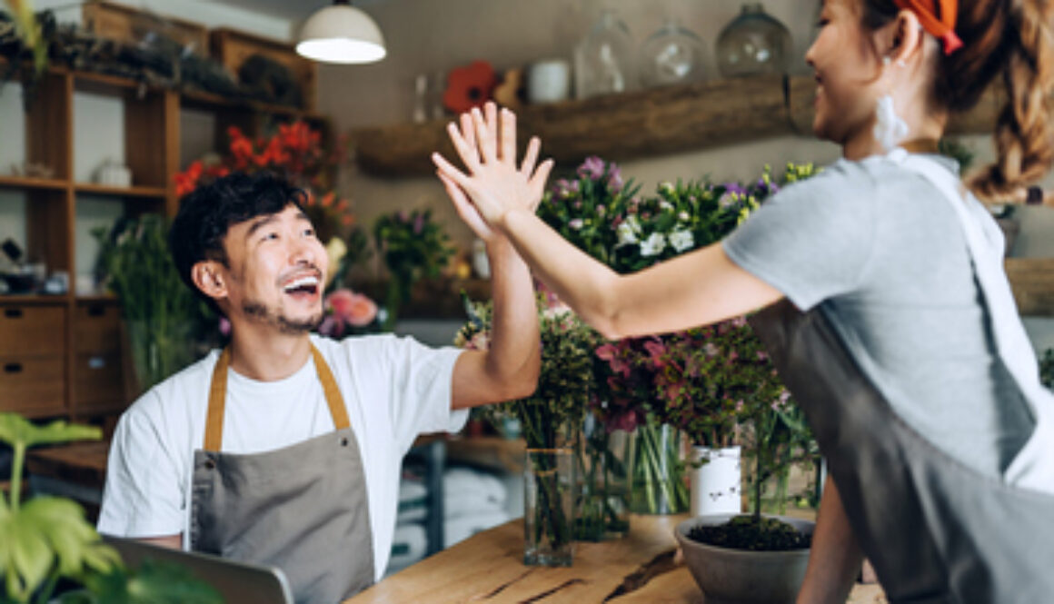 Cheerful young Asian couple, owners of small business flower shop, working together as a team, giving each other a high five in the shop. Start-up business, business partnership and teamwork. Working together for successful business