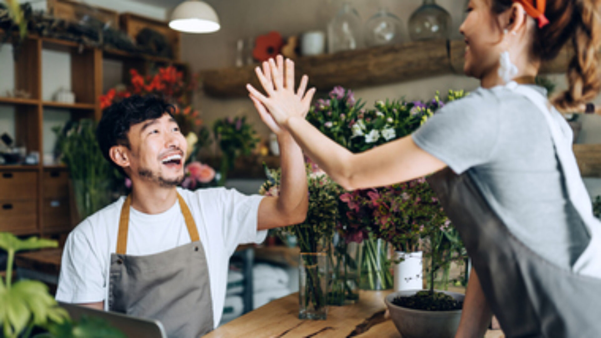 Cheerful young Asian couple, owners of small business flower shop, working together as a team, giving each other a high five in the shop. Start-up business, business partnership and teamwork. Working together for successful business