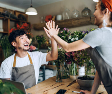 Cheerful young Asian couple, owners of small business flower shop, working together as a team, giving each other a high five in the shop. Start-up business, business partnership and teamwork. Working together for successful business