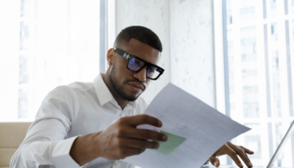Serious African American manager in stylish glasses reading corporate document