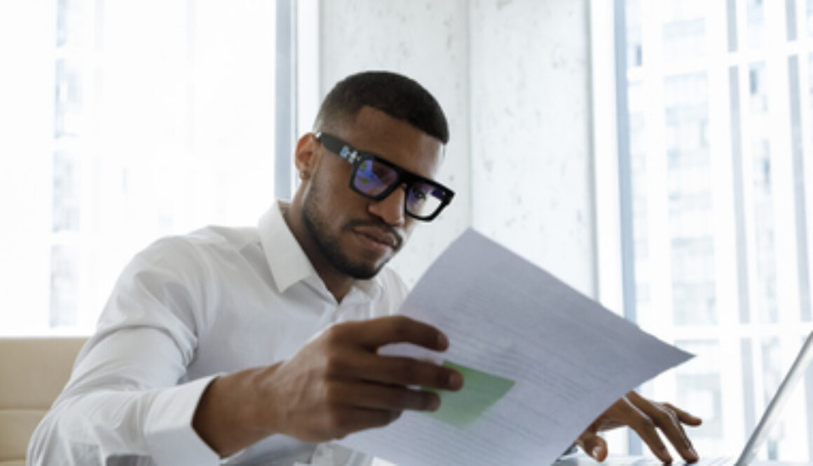 Serious African American manager in stylish glasses reading corporate document